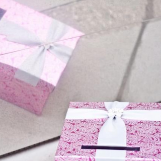 custom card box for an Indian wedding constructed out of magenta paper, along with silver silk ribbon and a brooch outdoors at the event, displayed beautifully for guests to use 