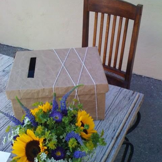 custom card box constructed out of textured brown paper and cotton jute displayed at a baby shower on a rustic table along with sweet floral arrangement of sunflowers  