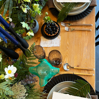 forest inspired wedding table setting full of moss shade plates, bowls, and glasses displays one glass draped with silk drink charm in emerald-green with golden glass cube beads