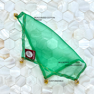 Detailed view of a luxurious emerald-green silk cocktail veil adorned with golden cube beads, displayed elegantly on white seashell tile