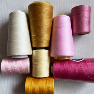 array of mercerized cotton threads varying in shades from nude, ecru, to golden, dust rose, merlot, pink